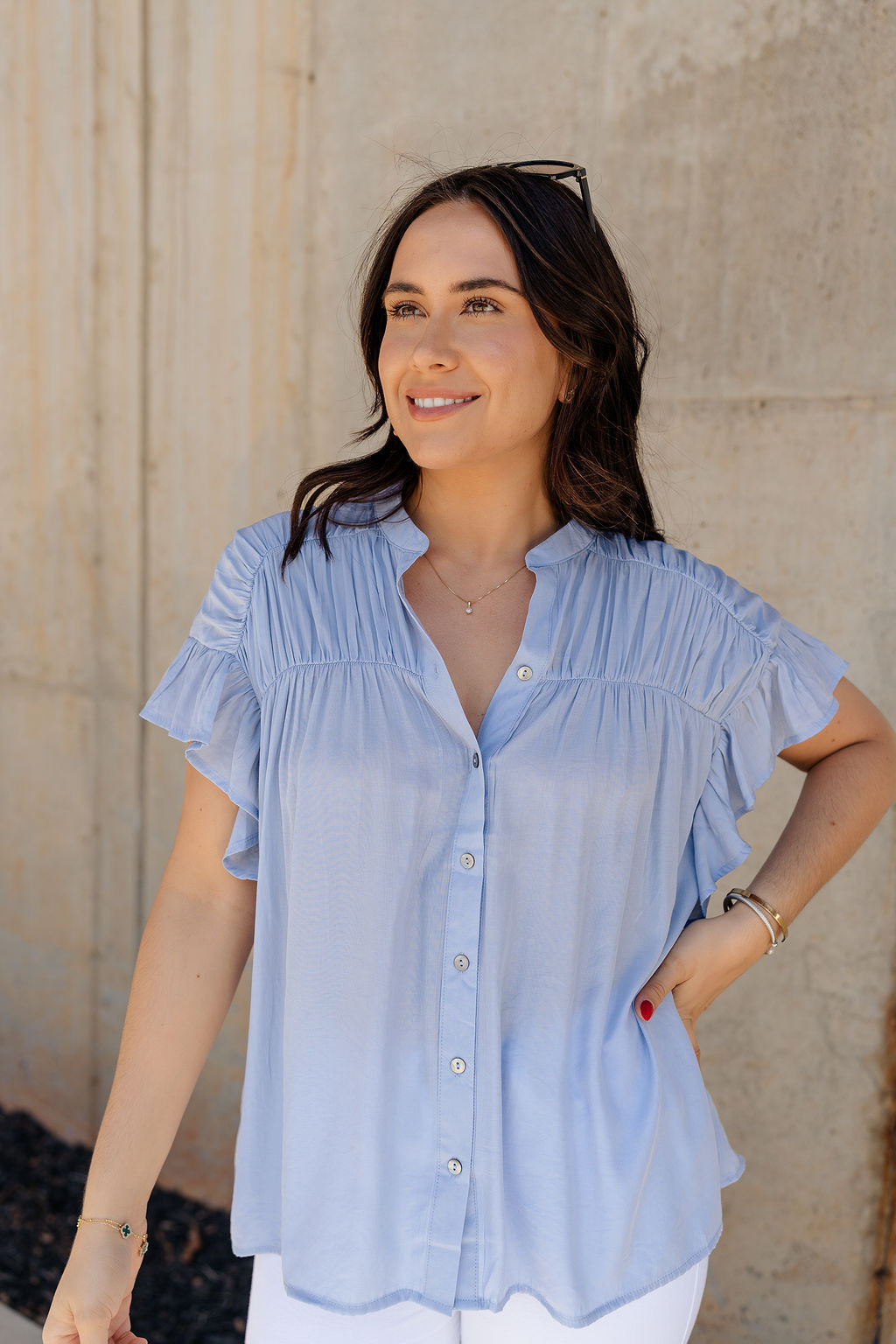 Front view of model wearing the Kennedy Light Blue Button-Up Top which features light blue fabric, monochrome button up front closure, round neckline with v-neckline cutout and short ruffle sleeves.