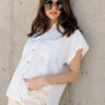 Front view of model wearing the Claire Off White Collared Short Sleeve Top which features white fabric, a front chest pocket, short sleeves with cuffs, small side slits, a button-up front, and a collared neckline.