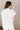 Back view of model wearing the Claire Off White Collared Short Sleeve Top which features white fabric, a front chest pocket, short sleeves with cuffs, small side slits, a button-up front, and a collared neckline.