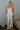 Full body view of model wearing the Celeste Ivory V-Wire Sleeveless Jumpsuit which features ivory knit fabric, full-length ivory lining, a structured notched neckline, thick straps, side pockets, and wide legs.