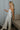 Full body side view of model wearing the Celeste Ivory V-Wire Sleeveless Jumpsuit which features ivory knit fabric, full-length ivory lining, a structured notched neckline, thick straps, side pockets, and wide legs.