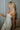 Side view of model wearing the Celeste Ivory V-Wire Sleeveless Jumpsuit which features ivory knit fabric, full-length ivory lining, a structured notched neckline, thick straps, side pockets, and wide legs.
