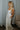 Full body side view of model wearing the Celeste Ivory V-Wire Sleeveless Jumpsuit which features ivory knit fabric, full-length ivory lining, a structured notched neckline, thick straps, side pockets, and wide legs.