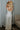 Full body back view of model wearing the Celeste Ivory V-Wire Sleeveless Jumpsuit which features ivory knit fabric, full-length ivory lining, a structured notched neckline, thick straps, side pockets, and wide legs.