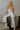 Full body view of model wearing the Celeste Ivory V-Wire Sleeveless Jumpsuit which features ivory knit fabric, full-length ivory lining, a structured notched neckline, thick straps, side pockets, and wide legs.