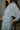 Close-up side view of model wearing the semi-sheer ivory fabric with subtle plaid texture, an abstract blue and green print, shimmer thread details, a surplice neckline, an elastic waist, a layered skirt, un-lined 3/4 sleeves with button closures, and ivory lining in the top and skirt.