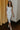 Full body view of model wearing the Camila Cream Denim Button-Up Midi Dress which features  cream denim fabric, contrast stitching, a button-up front with silver button closures, side and back pockets, a sweetheart neckline, thick straps, and a midi-length hem.