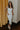 Full body view of model wearing the Camila Cream Denim Button-Up Midi Dress which features  cream denim fabric, contrast stitching, a button-up front with silver button closures, side and back pockets, a sweetheart neckline, thick straps, and a midi-length hem.
