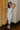 Full body view of model wearing the Camila Cream Denim Button-Up Midi Dress which features  cream denim fabric, contrast stitching, a button-up front with silver button closures, side and back pockets, a sweetheart neckline, thick straps, and a midi-length hem.