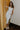 Full body view of model wearing the Camila Cream Denim Button-Up Midi Dress which features  cream denim fabric, contrast stitching, a button-up front with silver button closures, side and back pockets, a sweetheart neckline, thick straps, and a midi-length hem.
