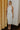Full body view of model wearing the Elisya Cream Ruched Midi Dress which features cream sheen knit fabric, midi length, cream lining, slit on the side, ruched side details, high neckline and sleeveless.