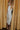 Full body view of model wearing the Elisya Cream Ruched Midi Dress which features cream sheen knit fabric, midi length, cream lining, slit on the side, ruched side details, high neckline and sleeveless.