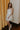 Full body front view of model wearing the Angelica Cream Sheer Floral Dress that features cream mesh fabric with a light green leaf pattern and embroidered white and gold flowers, cream lining, a smocked top, and adjustable spaghetti straps.
