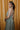 Side view of model wearing the Cleo Green & White Halter Twist Midi Dress which features white and green lightweight fabric, geometric design, maxi length, halter twist neckline, sleeveless and open back with monochrome back zipper with hook closure.
