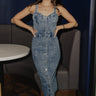 Full body view of model wearing the Lucia Acid Indigo Denim Midi Dress which features acid medium wash denim fabric, midi length, silver button-up front closure, slit in the back, two back pockets, belt loops, sweetheart neckline, straps and open back.