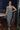 Full body view of model wearing the Lucia Acid Indigo Denim Midi Dress which features acid medium wash denim fabric, midi length, silver button-up front closure, slit in the back, two back pockets, belt loops, sweetheart neckline, straps and open back.
