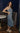 Full body side view of model wearing the Lucia Acid Indigo Denim Midi Dress which features acid medium wash denim fabric, midi length, silver button-up front closure, slit in the back, two back pockets, belt loops, sweetheart neckline, straps and open back.