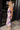 Full body side view of model wearing the Isla Multi Swirl Midi Dress which features purple, fuchsia, peach, yellow, green, light pink and white knit fabric, wattercolor swirl print, peach lining, mid length, v-neckline, thick straps and sleeveless.