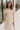 Front view of model wearing the Daphne Oatmeal Button-Up Midi Dress which features beige fabric, a button-up front with pearlescent buttons, a collared neckline, short sleeves with cuffs and button tabs, and a rounded midi hemline.