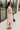Full body side view of model wearing the Daphne Oatmeal Button-Up Midi Dress which features beige fabric, a button-up front with pearlescent buttons, a collared neckline, short sleeves with cuffs and button tabs, and a rounded midi hemline.