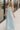 Full body view of model wearing the Gillie Light Blue Halter Maxi Dress which features light blue and yellow knit textured fabric, light blue lining, small gingham print design, maxi length, halter neckline, adjustable straps, sleeveless and open back.