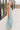 Full body side view of model wearing the Gillie Light Blue Halter Maxi Dress which features light blue and yellow knit textured fabric, light blue lining, small gingham print design, maxi length, halter neckline, adjustable straps, sleeveless and open back.