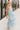 Full body side view of model wearing the Gillie Light Blue Halter Maxi Dress which features light blue and yellow knit textured fabric, light blue lining, small gingham print design, maxi length, halter neckline, adjustable straps, sleeveless and open back.
