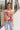 Front view of model wearing the Bianca Satin Floral Tank Top that has sage green satin fabric with a green, purple, pink, yellow, and red floral print and a halter neckline with 3 back button closures. Top is shown untucked.