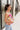 Side view of model wearing the Bianca Satin Floral Tank Top that has sage green satin fabric with a green, purple, pink, yellow, and red floral print and a halter neckline with 3 back button closures. Top is shown untucked.