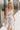 front view of model wearing the Gwen White Floral Mini Dress that features white fabric with a peach, brown, green, blue, and purple floral print, adjustable spaghetti straps, a smocked back with a zipper and hook closure, a flared skirt with a structured hemline, and white lining.