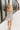 Full body back view of model wearing the Gwen White Floral Mini Dress that features white fabric with a peach, brown, green, blue, and purple floral print, adjustable spaghetti straps, a smocked back with a zipper and hook closure, a flared skirt with a structured hemline, and white lining.