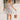 Full body front view of model wearing the Gwen White Floral Mini Dress that features white fabric with a peach, brown, green, blue, and purple floral print, adjustable spaghetti straps, a smocked back with a zipper and hook closure, a flared skirt with a structured hemline, and white lining.