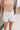 he girl model is wearing white denim shorts with a frayed hem. This is a front  shot of her wearing the shorts with a tan tank top.