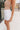 he girl model is wearing white denim shorts with a frayed hem. This is a side shot of her wearing the shorts with a tan tank top.