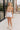 The girl model is wearing white denim shorts with a frayed hem.  This is a front shot of her wearing the shorts with a tan tank top. 