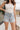 Close-up front view of female brunette model wearing the light wash color of the Hayden Frayed Hem Denim Shorts, paired with a white tank top.