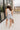 Full body back view of female brunette model wearing the light wash color of the Hayden Frayed Hem Denim Shorts, paired with a white tank top.