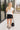 Full body front view of female model wearing the Dana Black Frayed Hem Denim Shorts that feature black distressed denim, frayed hems, and pockets. Paired with white top.