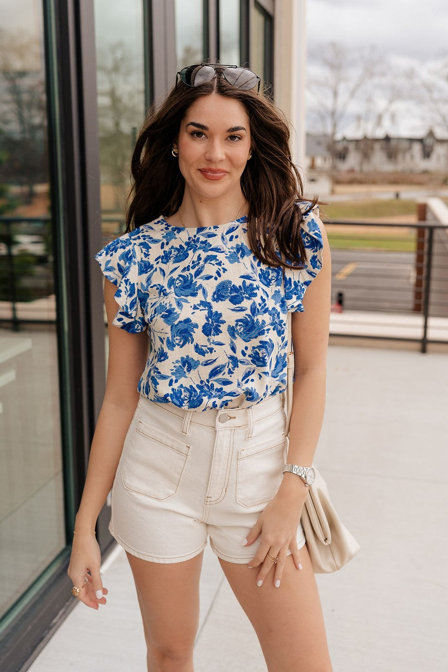 Front view of female brunette model wearing the Mckenzie Off White Denim Shorts that feature off white denim, contrast stitching, pockets, and a high rise. Styled with blue and white floral top.