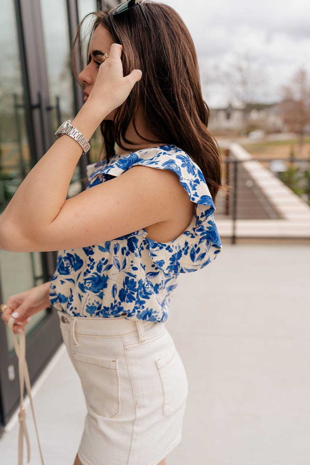 Side view of model wearing the Carmen Blue & Cream Floral Top which features blue and cream knit fabric, floral pattern, round neckline, ruffle short sleeves and keyhole back with button closure.