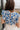 Close up back view of model wearing the Carmen Blue & Cream Floral Top which features blue and cream knit fabric, floral pattern, round neckline, ruffle short sleeves and keyhole back with button closure.