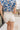 Back view of female brunette model wearing the Mckenzie Off White Denim Shorts that feature off white denim, contrast stitching, pockets, and a high rise. Styled with blue and white floral top.