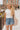 Front view of female blonde model wearing the medium wash color of the Hayden Frayed Hem Denim Shorts, paired with a white cropped t-shirt.