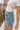 Close side view of female blonde model wearing the medium wash color of the Hayden Frayed Hem Denim Shorts, paired with a white cropped t-shirt.