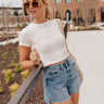 Front view of female blonde model wearing the medium wash color of the Hayden Frayed Hem Denim Shorts, paired with a white cropped t-shirt.