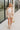 Full body front view of model wearing the Cassidy Beige Gauze Shorts that feature beige gauze fabric, an elastic drawstring waist, side pockets, and frayed hem details.