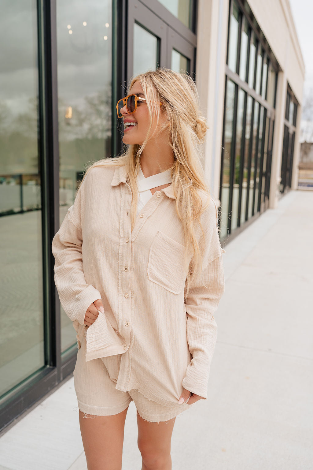  front view of model wearing the Cassidy Beige Gauze Long Sleeve Top that features beige gauze fabric, a button-up front with beige button closures, a collared neckline, a left front chest pocket, drop shoulder long sleeves, and frayed hem details. 