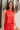 Front view of model wearing the Vada Red Tank Top that features red woven fabric with raw frayed hems, a round neckline, a sleeveless body, small side slits, and a keyhole back with a button closure.