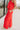 Side view of model wearing the Vada Red Wide Leg Pants that feature red woven fabric, side pockets, an elastic waistband, and flowy wide legs.