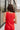 Back view of model wearing the Vada Red Tank Top that features red woven fabric with raw frayed hems, a round neckline, a sleeveless body, small side slits, and a keyhole back with a button closure.